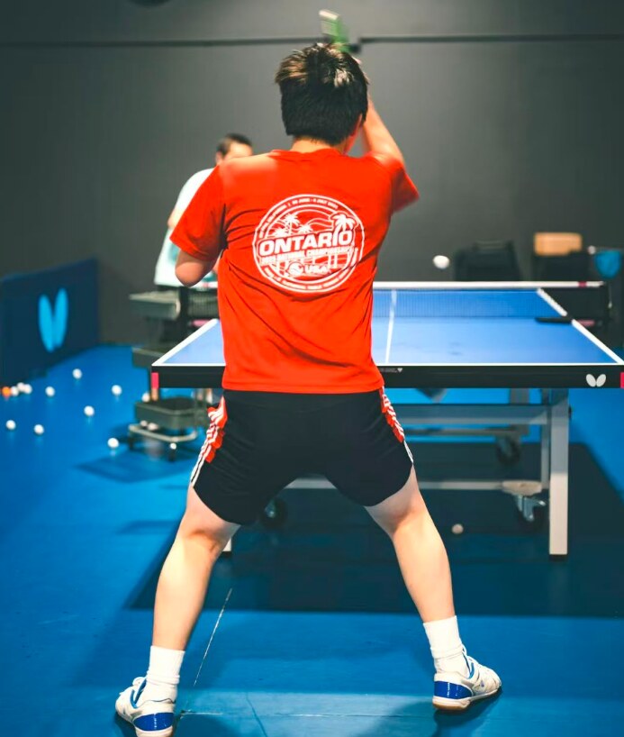 Table tennis player in a red shirt on an indoor court at Eric Table Tennis Academy.