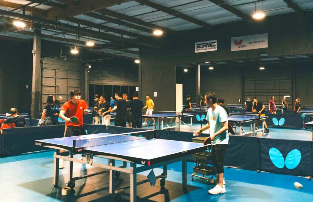 Multiple tables and players inside the training area at Eric Table Tennis Academy.